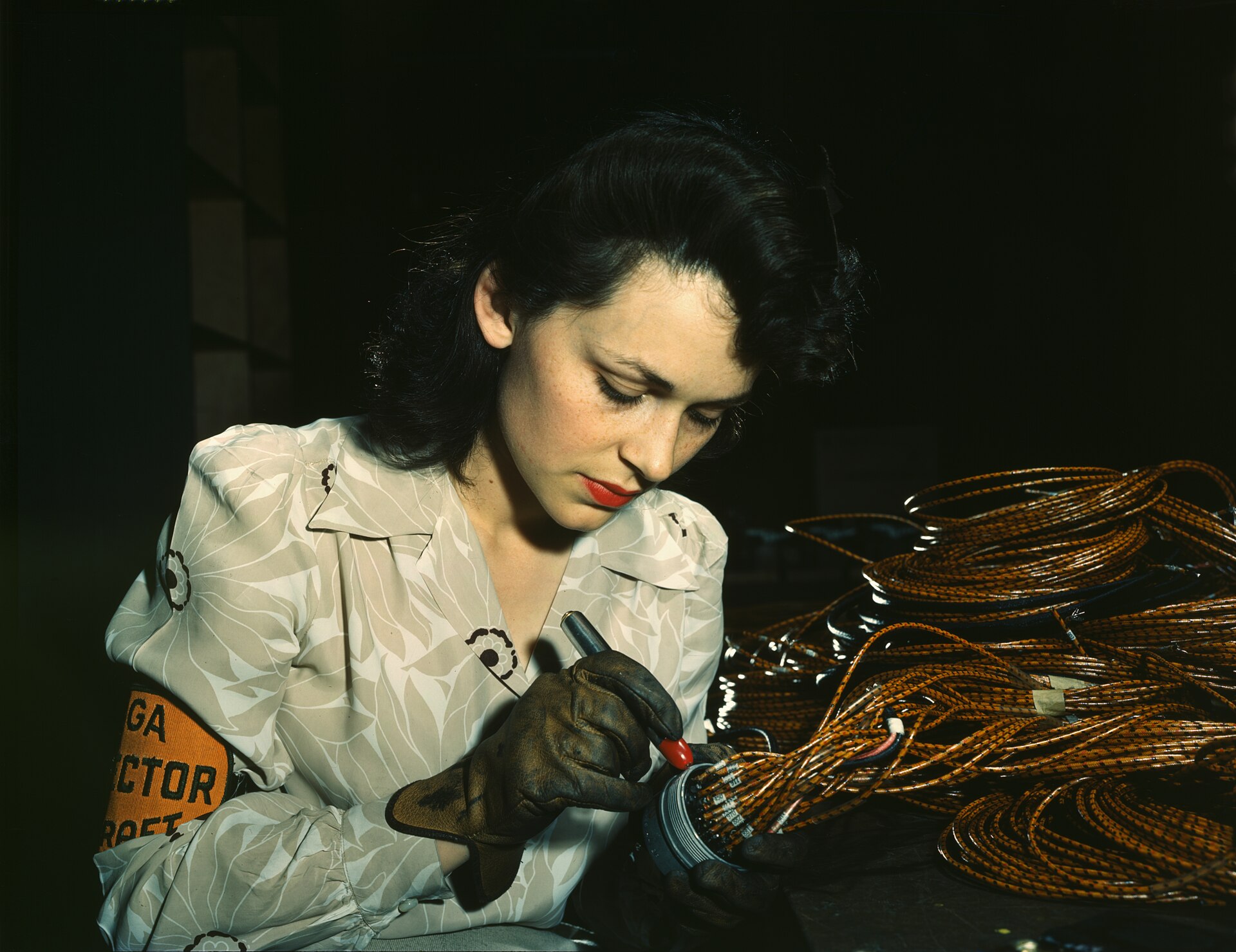 An aircraft worker wearing an inspector armband checking the ends of a bundle of wiring.